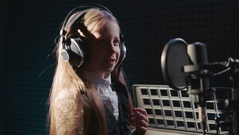 attentive girl waits for signal for recording. child in headphones listens attentively to teacher instruction before recording song in insulated room