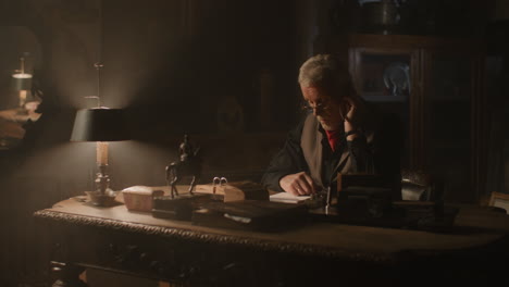 older passionate man evaluates an old watch in his office at night