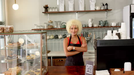 biracial barista with curly blonde hair stands at coffee shop counter