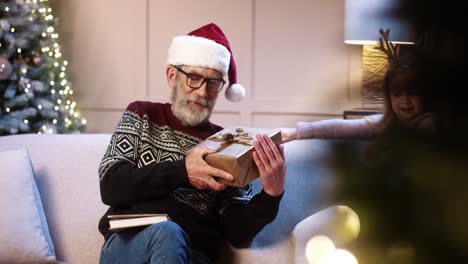 heureuse mignonne petite fille et garçon donnant des cadeaux au vieux grand-père assis dans une maison confortablement décorée près de l'arbre du nouvel an et lisant un livre