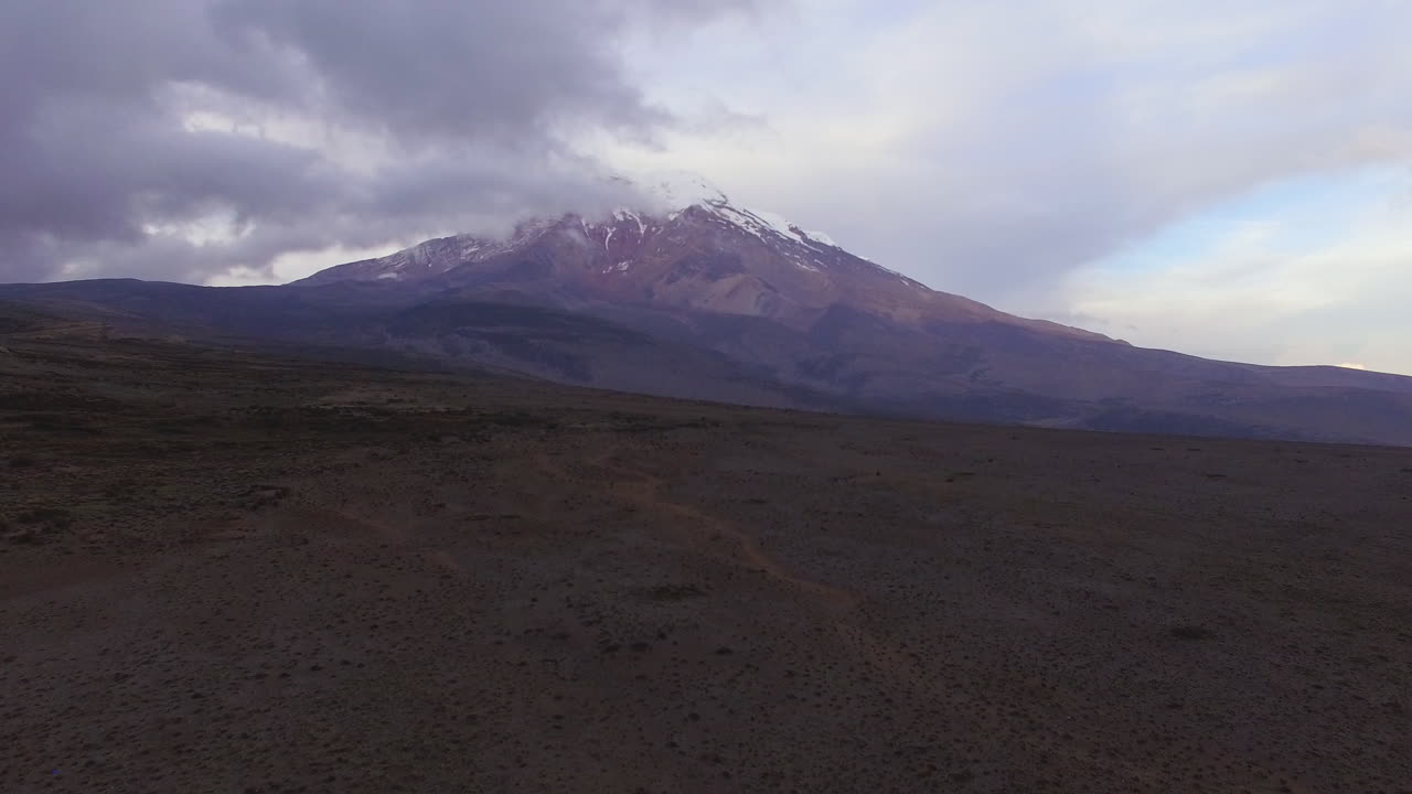 toma aérea que se eleva desde un plano volcánico para mostrar el cotopaxi parcialmente oculto por nubes oscuras