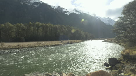 running river surrounded by snow capped mountains and lush green forrest on a sunny winters day in new zealand