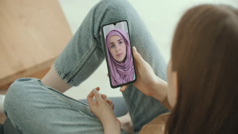 Frau-Nutzt-Medizinische-App-Auf-Dem-Smartphone-Und-Berät-Sich-Per-Videokonferenz-Mit-Einer-Arabischen-Muslimischen-Frau-Im-Hijab-Arzt.-Frau-Nutzt-Online-Chat,-Um-Mit-Familientherapeuten-Und-Einer-Coronavirus-Pandemie-Zu-Sprechen.