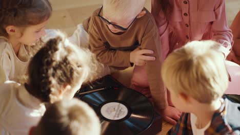 preschool children sit around a special record player listening to music and communicating with each other in a sunny cozy room in a club to prepare children for school