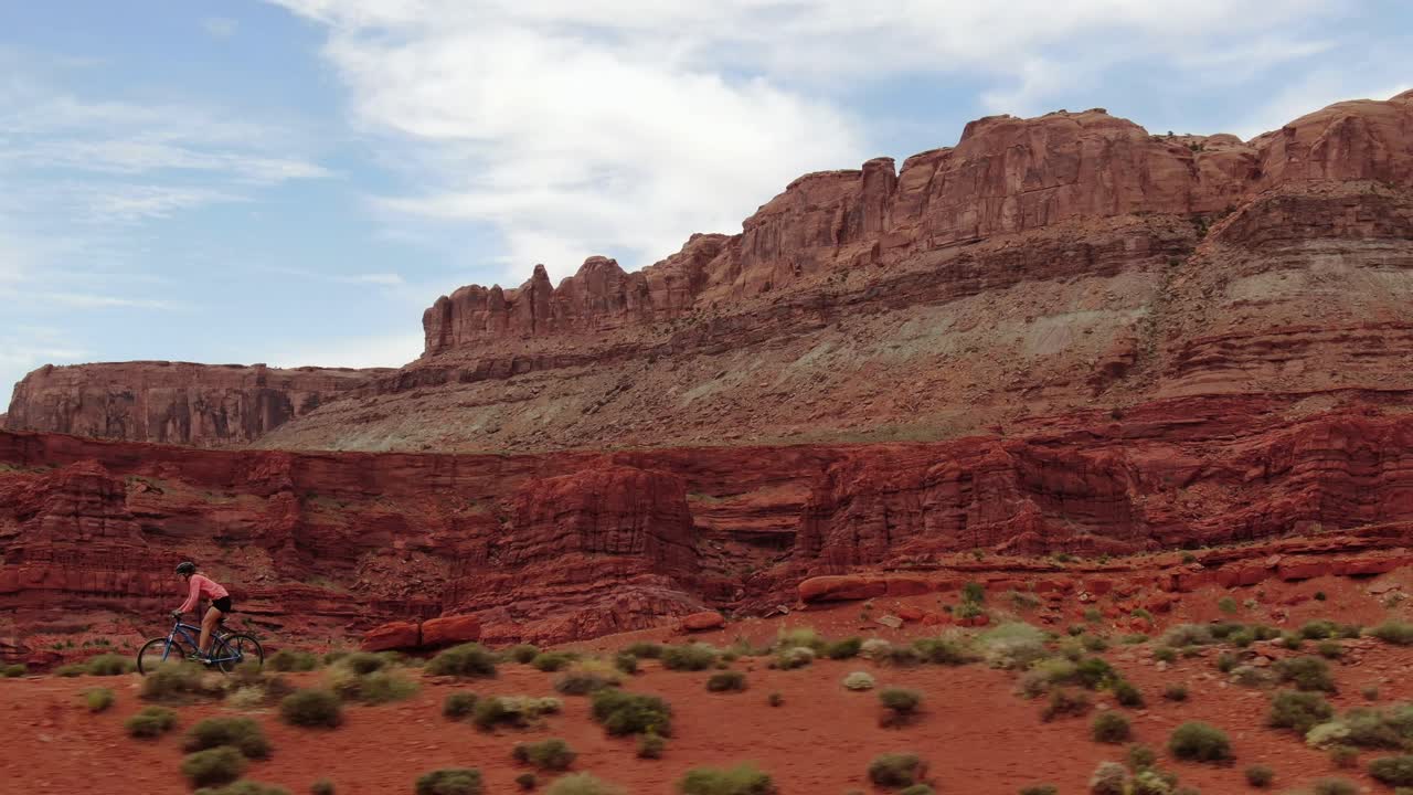 가파른 산 절벽이 있는 트레일에서 여성 산악 자전거 타는 사람의 공중 트럭 왼쪽 샷