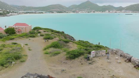 forward moving aerial view of old fort amsterdam at saint martin and revealing beautiful landscape at background with turquoise sea in front