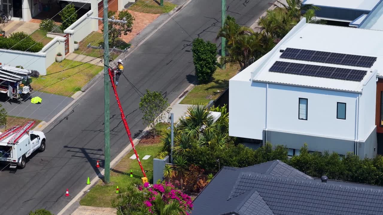 Aerial view of utility lineman on elevated platform servicing power pole in sunny suburb
