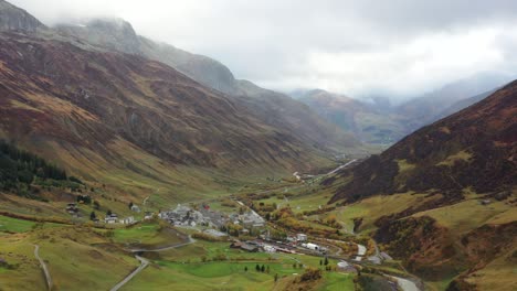 rainy-Aerial-View-on-Grimselpass-high-mountian-alpine-road,-river,-houses-and-Swiss-Alps-in-background