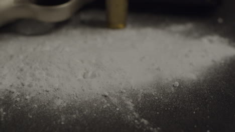primer plano de polvo de cocaína y una pistola y una bala en el fondo