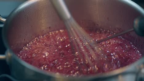 woman stirs boiling red berry caramel with small whisk