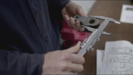 worker measuring metal part with caliper