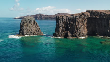 roque partido, gran canaria: aerial view in orbit over the large rock, with a great blue color of the sea