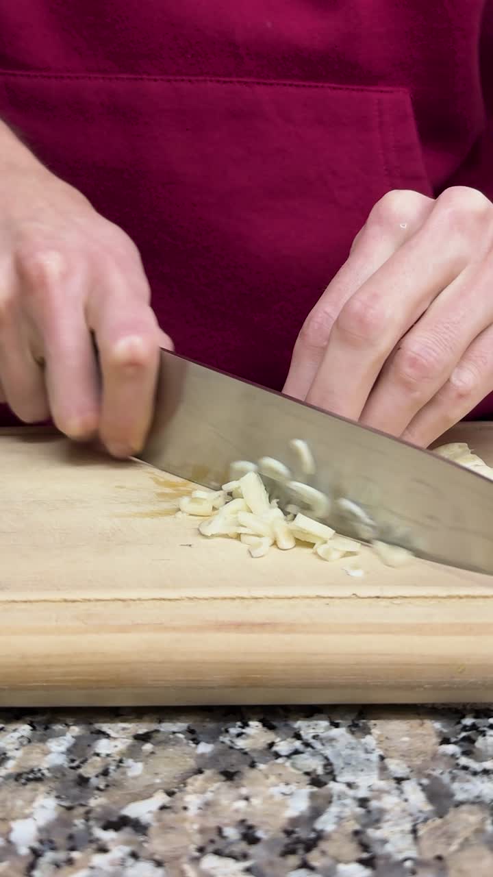 Vertical close up shot of a man chopping garlic cloves on a wooden table