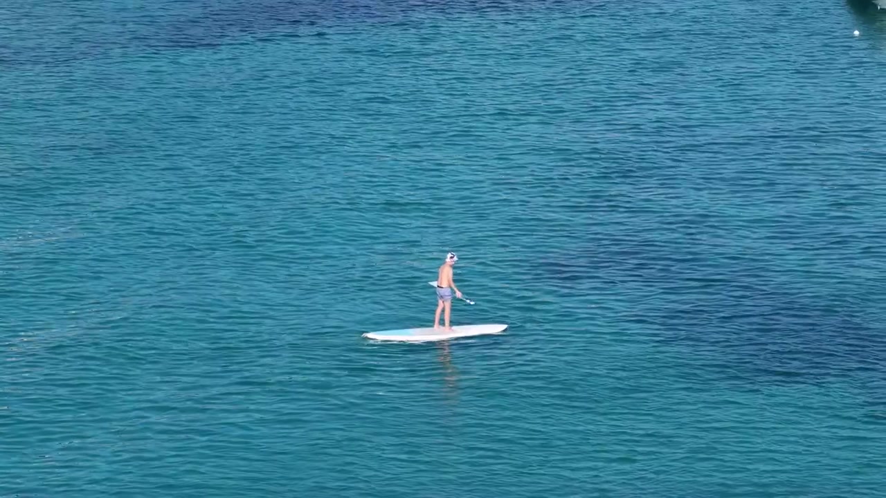 Pemandangan Drone Seorang Pria Ber-Stand Up Paddleboarding di Atas Perairan Laut Mediterania Biru Tua di Pantai Agios Georgios Pagon, Corfu Utara, Yunani.