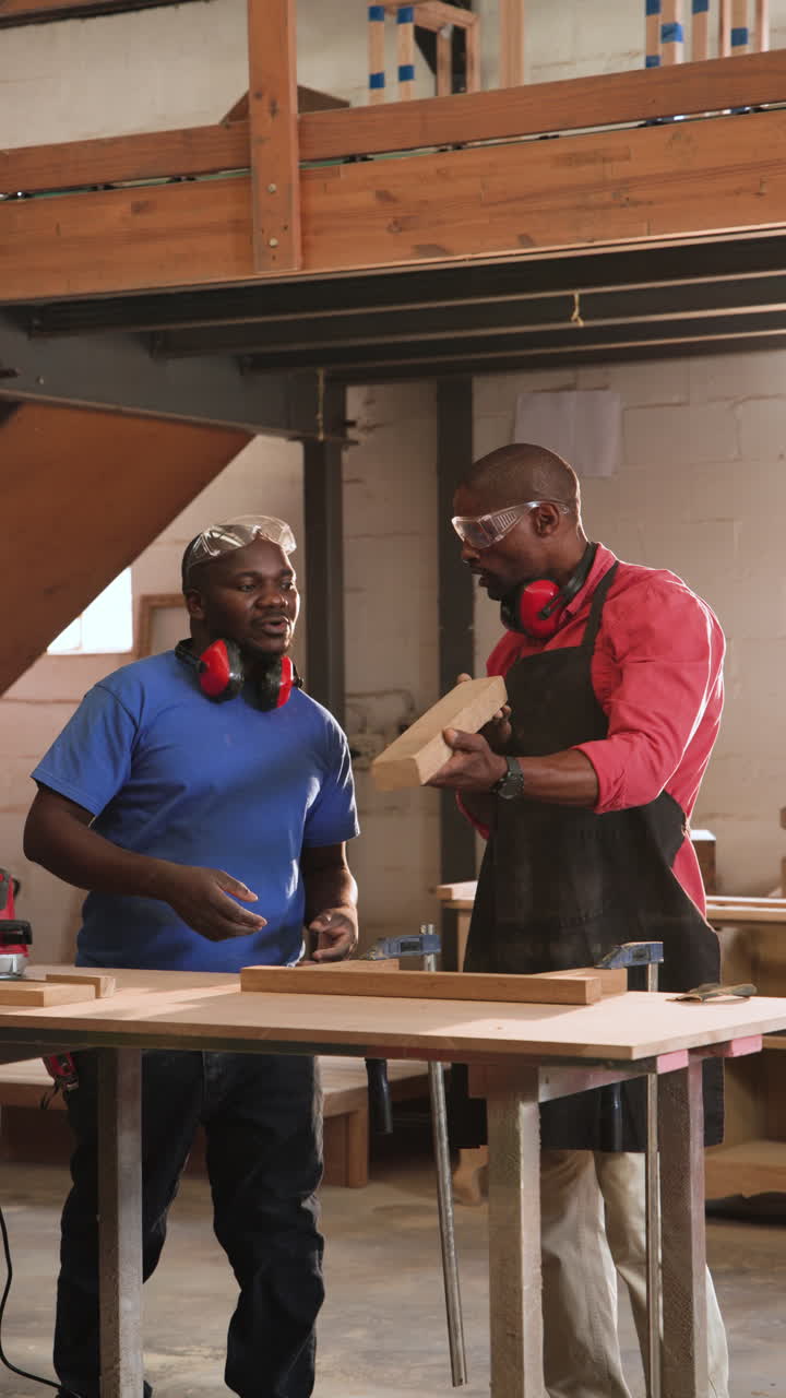 Vertical video: Sunlight sparking African American men planing and sanding wood at workbench