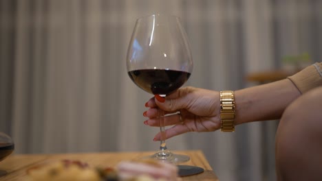 Manos-Femeninas-Levantando-Elegantemente-Una-Copa-De-Vino-Para-Brindar,-Capturando-La-Sofisticación-Y-El-Placer-De-Saborear-Una-Fina-Copa-De-Vino.