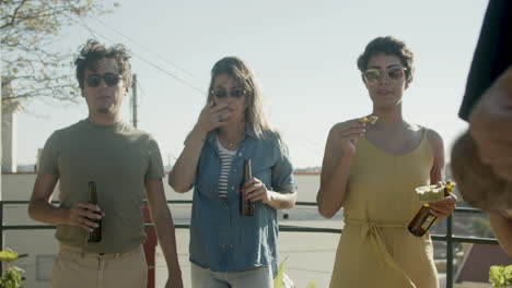 Carefree-man-and-women-standing-on-rooftop-and-eating-nachos