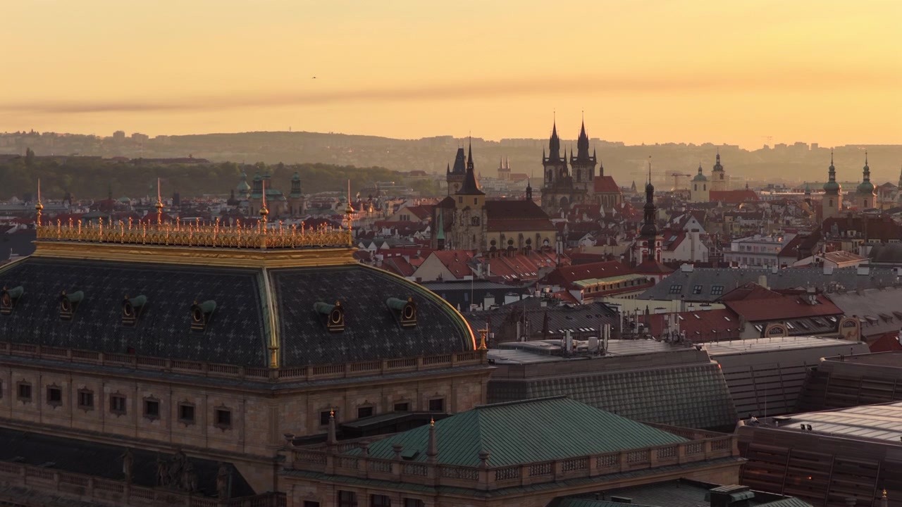 Vista aerea con drone sopra il tetto dorato e ornato del Teatro Nazionale verso le guglie della Chiesa di Tyn stagliate contro un'alba dorata e nebbiosa, Praga, Repubblica Ceca.