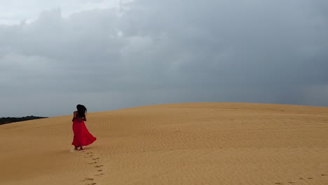 long hair hispanic woman in long red dress runs up huge sand dune