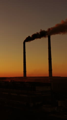 harmful factory among nature at sunset. dangerous smoke fills the air from industrial pipes. manufacturing at dusk. environment in danger. global warming. vertical video