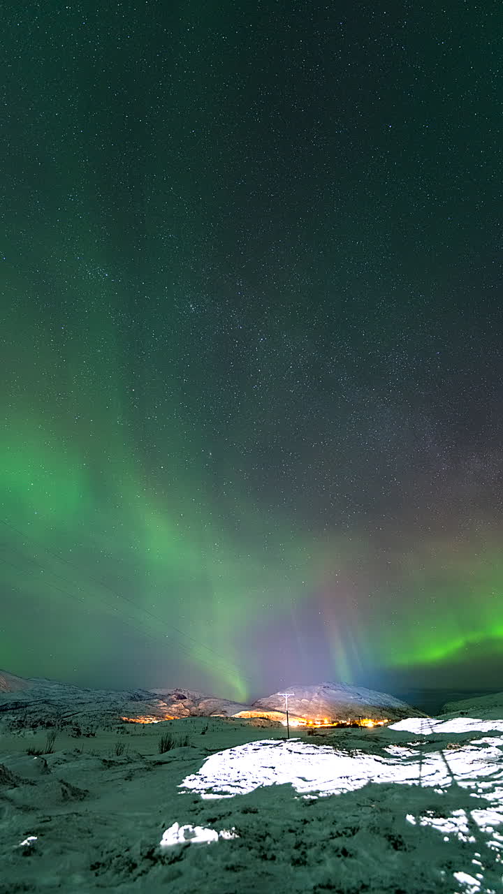 Brilliant aurora borealis over Norway’s Arctic landscape, casting a green glow on the rugged terrain as long tendrils sway in sky below stars