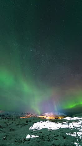brilliant aurora borealis over norway’s arctic landscape, casting a green glow on the rugged terrain as long tendrils sway in sky below stars