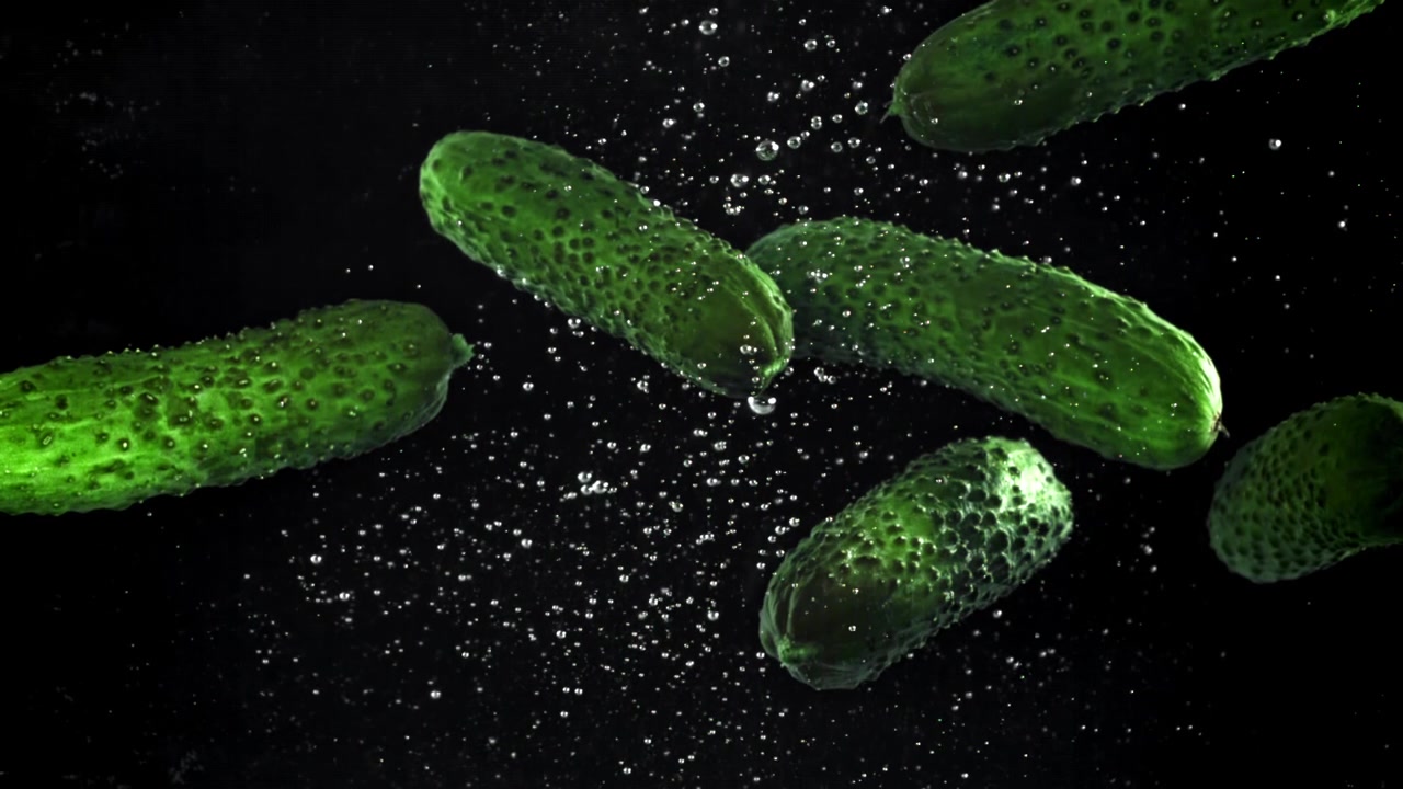 Cetrioli verdi freschi che galleggiano nell'acqua con bolle su sfondo nero