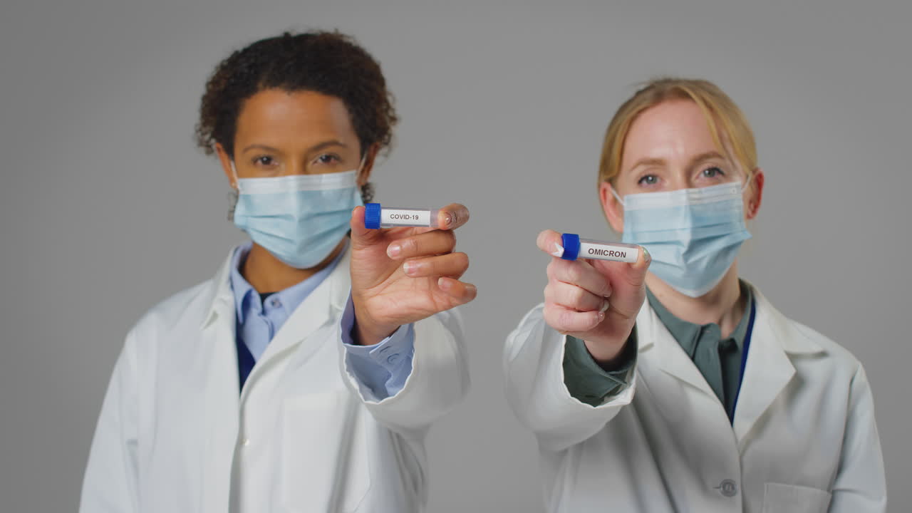 Studio Shot Of Lab Research Workers In Face Masks Holding Test Tubes Labelled Covid-19 And Omicron