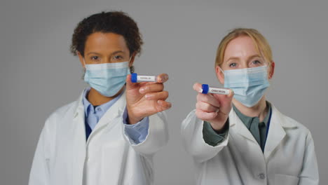 studio shot of lab research workers in face masks holding test tubes labelled covid-19 and omicron