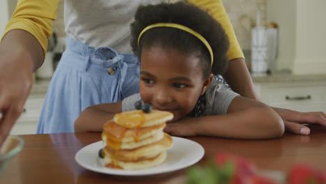 Happy-mother-with-daughter-decorating-pancakes-with-blueberries-in-kitchen