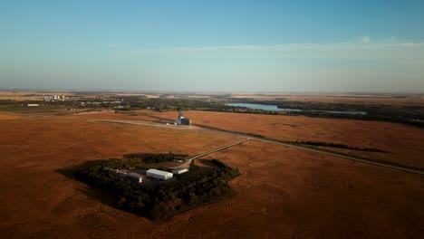 aerial drone shot blue sky over small canadian farm house and town in the middle of vast harvest blooming agriculture farmland fields