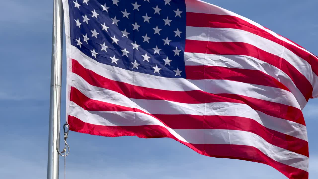 Aerial close up showing flag of United States against blue sky. Flying patriotic flag of USA. Symbol for peace and freedom on earth. Blowing flag on flagpole