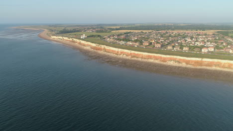 Establecimiento-De-Una-Toma-Aérea-Con-Drones-De-Los-Antiguos-Acantilados-Anaranjados-Y-Blancos-De-Hunstanton-Con-Faro-Y-Casas-En-Un-Día-Tranquilo-Con-Pequeñas-Olas-Al-Atardecer-En-El-Norte-De-Norfolk,-Reino-Unido