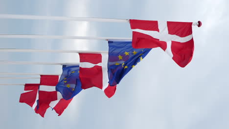 vertical shot of danish and european union flags on flagpoles flying with the wind