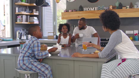 Family-Sitting-In-Kitchen-Enjoying-Morning-Breakfast-Together