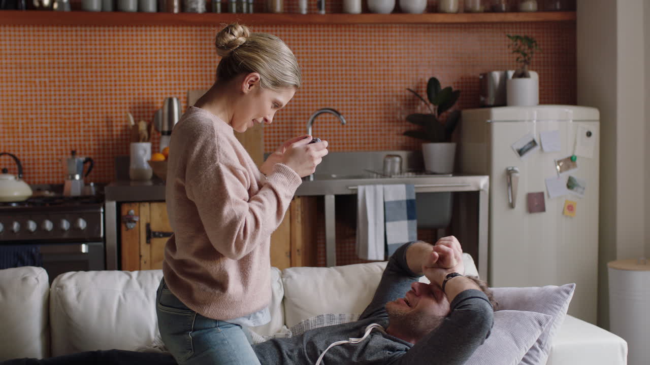 행복한 젊은 커플이 카메라를 사용하여 함께 사진을 찍고 소파에서 집에서 재미있게 로맨틱한 관계를 즐기며 서로 사진을 찍고 얼굴을 짓고 있습니다.