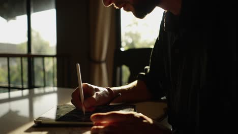 person using a digital tablet with a stylus, backlit by sunlight through a window