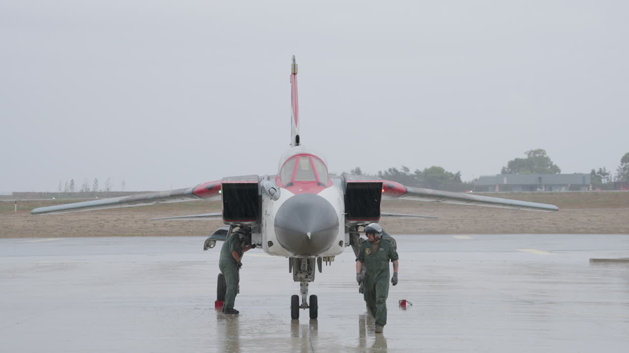 Piloti che ispezionano un caccia militare su una pista d'atterraggio piovosa