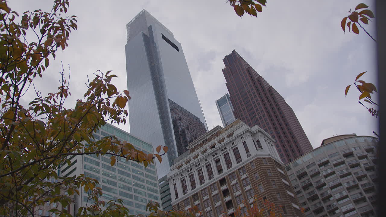 Slow-motion twist shot of a dramatic urban scene in Philadelphia, showcasing modern skyscrapers framed by autumn leaves, blending architectural grandeur with seasonal beauty and cinematic movement.