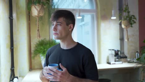 Young-european-Male-Student-is-enjoying-his-coffee-or-tea-at-the-coffeehouse-with-natural-background