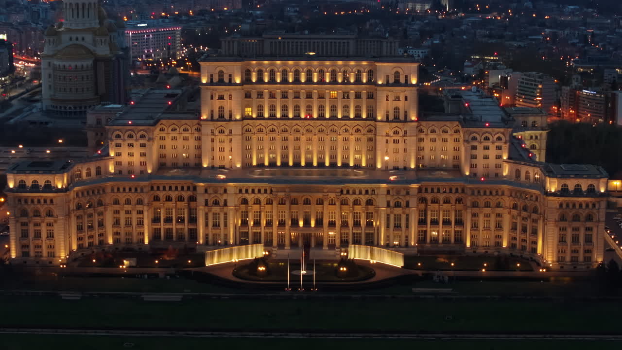Aerial drone view of illuminated Palace of the Parliament in Bucharest downtown in the evening. Multiple districts around. Romania