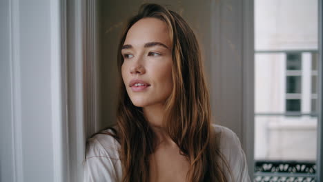 hermosa dama mirando por la ventana en el retrato interior beige. mujer mirando la calle