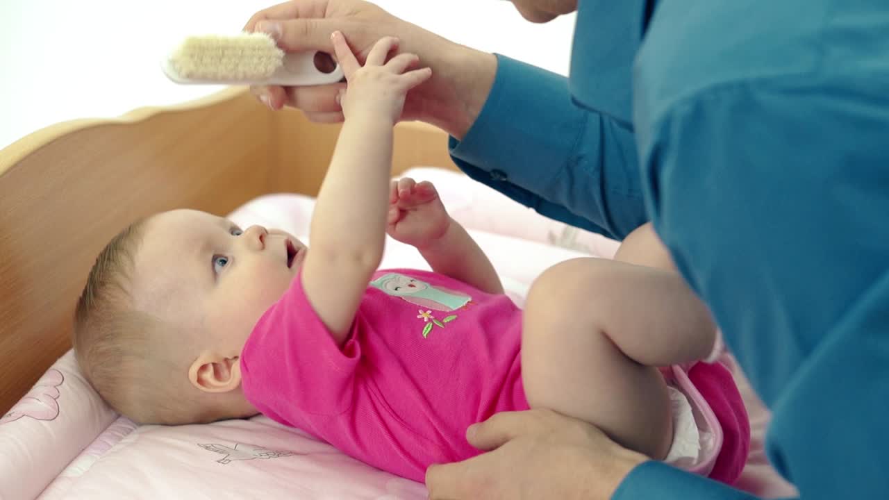 cu padre juega con la pequeña hija dulce que se acuesta en una mesa de cambio él peina cuidadosamente su cabello