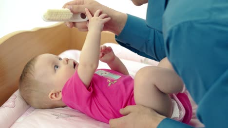 CU-father-plays-with-little-sweet-daughter-who-lies-on-a-changing-table-He-neatly-combs-her-hair