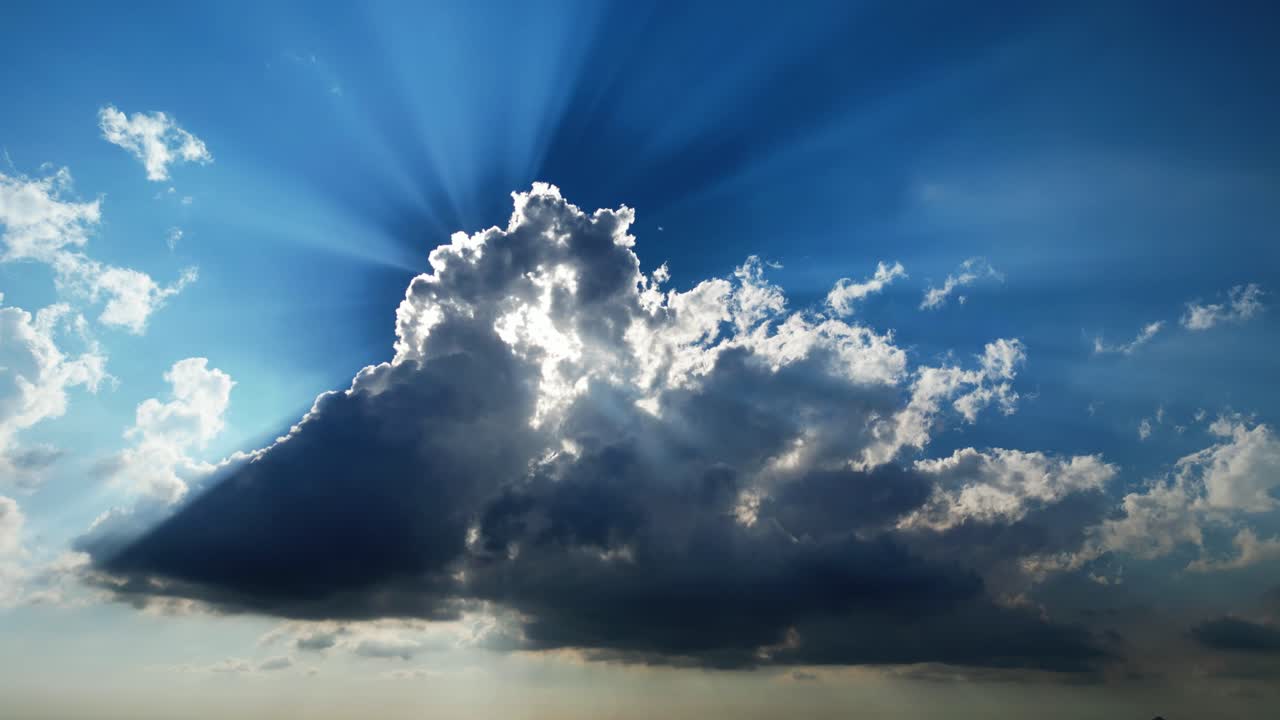 Nuvole che si muovono lentamente con raggi di sole radiosi che filtrano attraverso formazioni drammatiche in un cielo diurno blu brillante