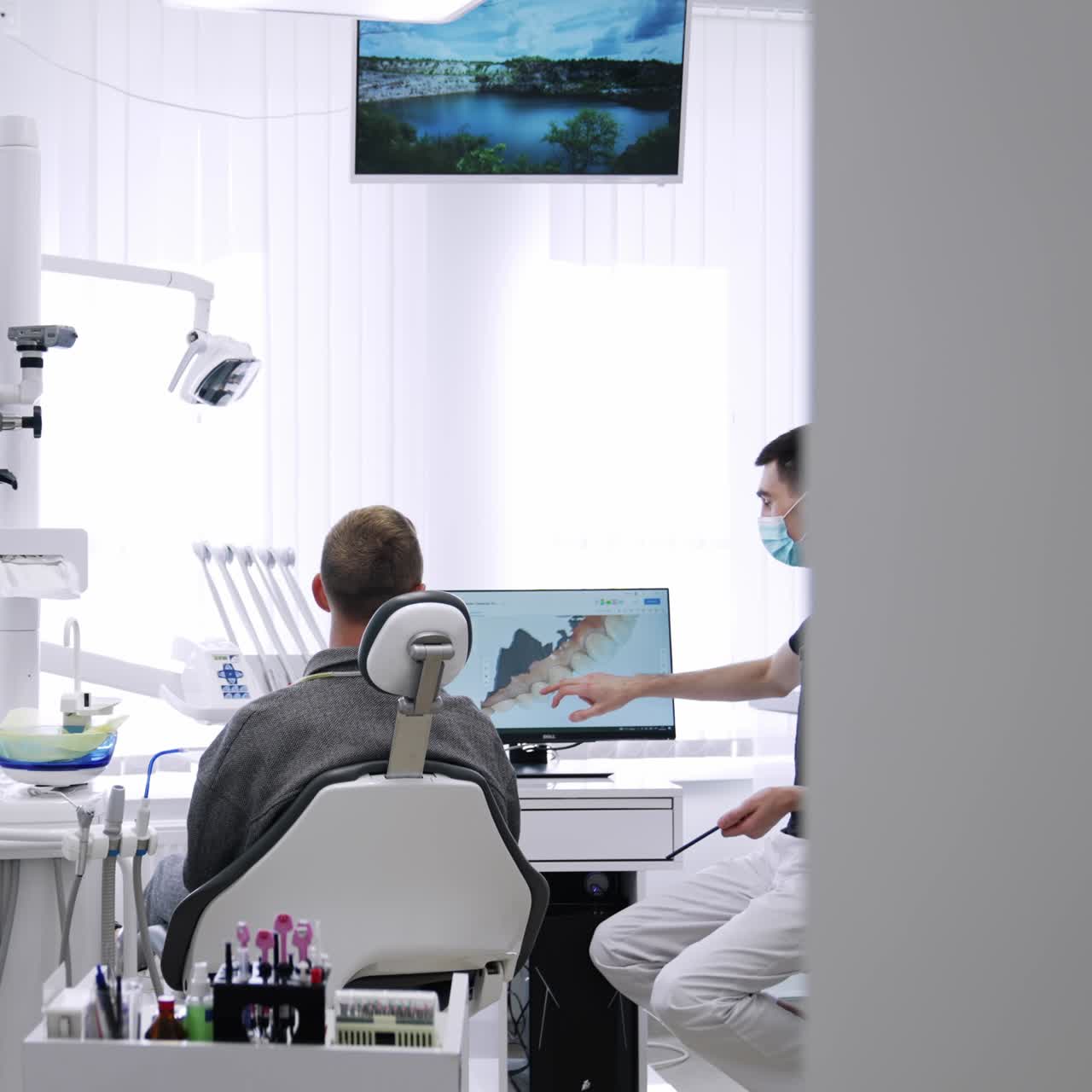 Modern well-equipped dentist's cabinet in clinics. Patient is shown his 3d image of teeth on the screen by a male dentist