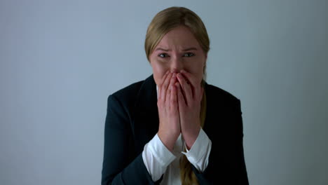 strongly stressed and scared woman in business clothes looks straight into the camera covering her face with her hands and almost crying