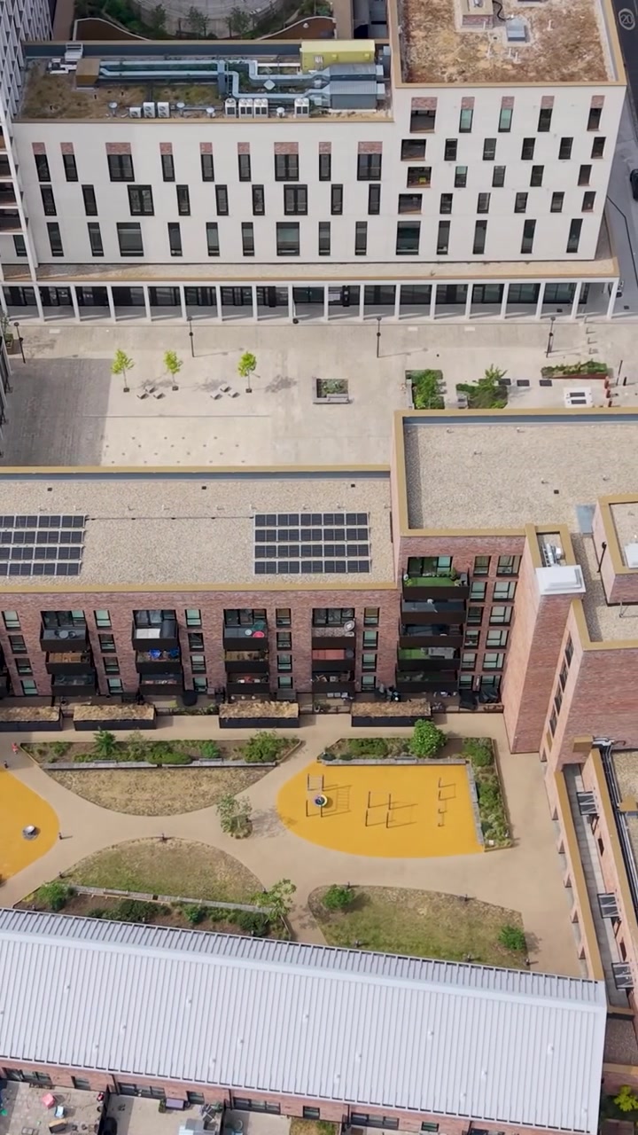Paneo vertical de dron hacia la derecha en Coronation Square, desde huertos comunitarios a través de apartamentos modernos hasta Coronation Gardens y parterres geométricos del parque, mostrando la regeneración urbana, calles y árboles