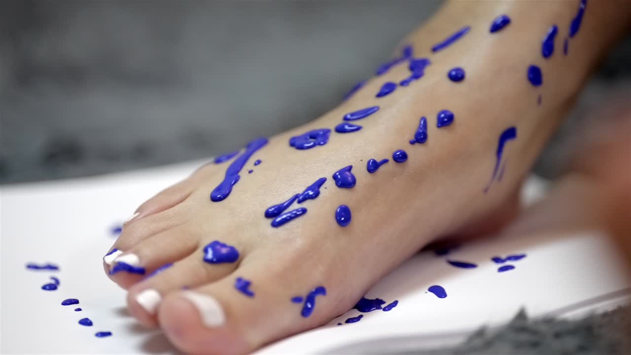 Gocce di vernice blu densa sul piede che creano un motivo a gocciolamento maculato sulla gamba femminile