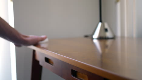 a hand cleaning dust and germs off of wood furniture with an antibacterial disinfecting wipe to keep healthy and safe from covid 19 corona virus or bacteria during pandemic